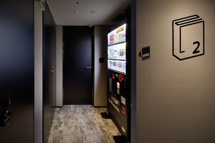 A hallway with a vending machine, a door, and a wall with a number sign.