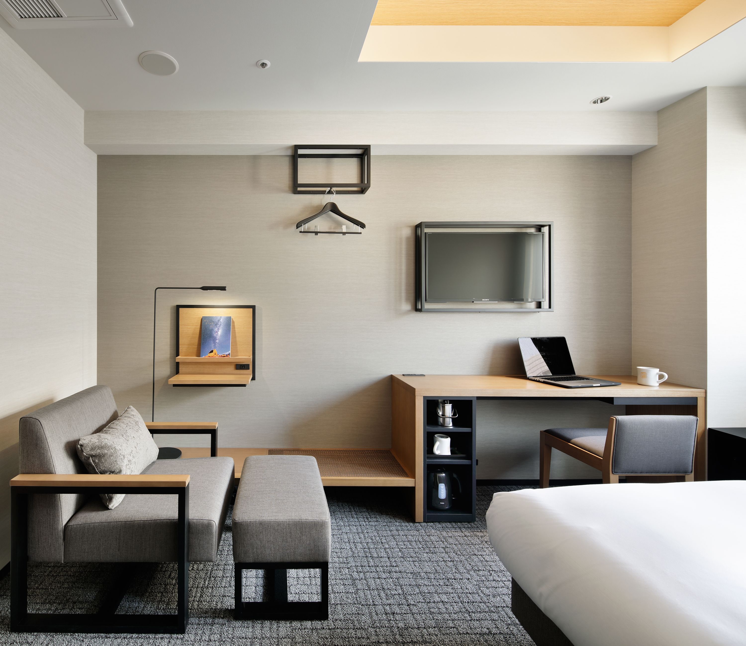 Ein modernes Hotelzimmer mit einem Bett, einem Schreibtisch mit Laptop, einem Fernseher, einer Couch und einem Couchtisch.
