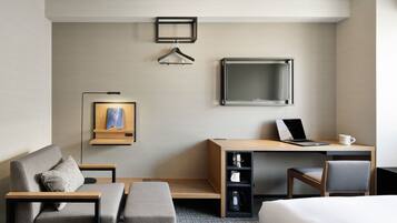 Ein modernes Hotelzimmer mit einem Bett, einem Schreibtisch mit Laptop, einem Fernseher, einer Couch und einem Couchtisch.