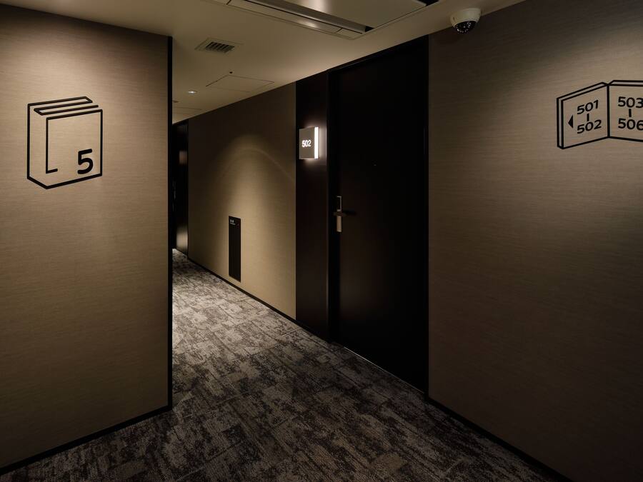 A hallway with carpeted floors, a door labeled '502', and a sign with room numbers '501', '502', '503', '506'.