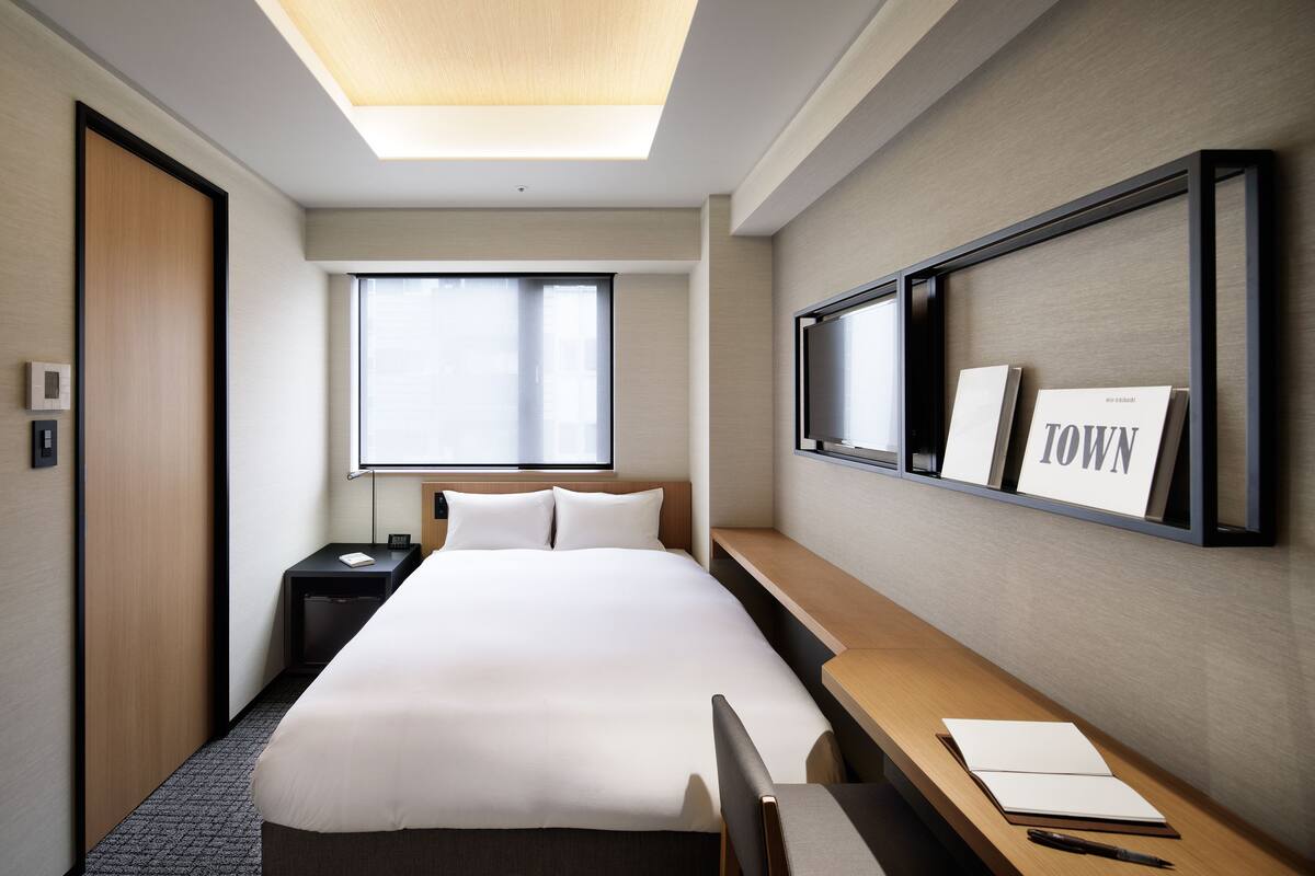 Habitación de hotel con una cama grande, un escritorio, una silla, una mesita de noche, una ventana y un cuadro en la pared.