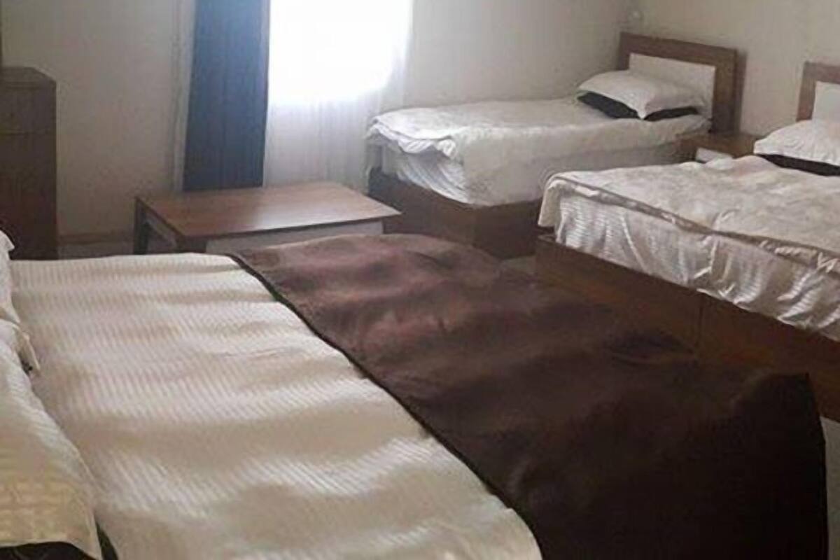 Ein Zimmer mit zwei Einzelbetten, einem kleinen Tisch und einem Fenster mit Vorhängen.
