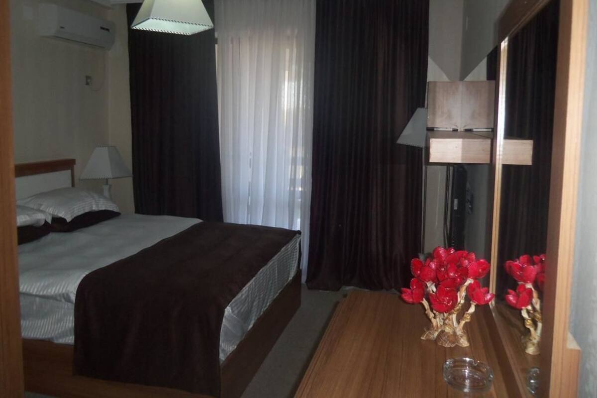 Ein Hotelzimmer mit einem Bett, einem Holzschrank, einem Spiegel und einer Vase mit roten Blumen.