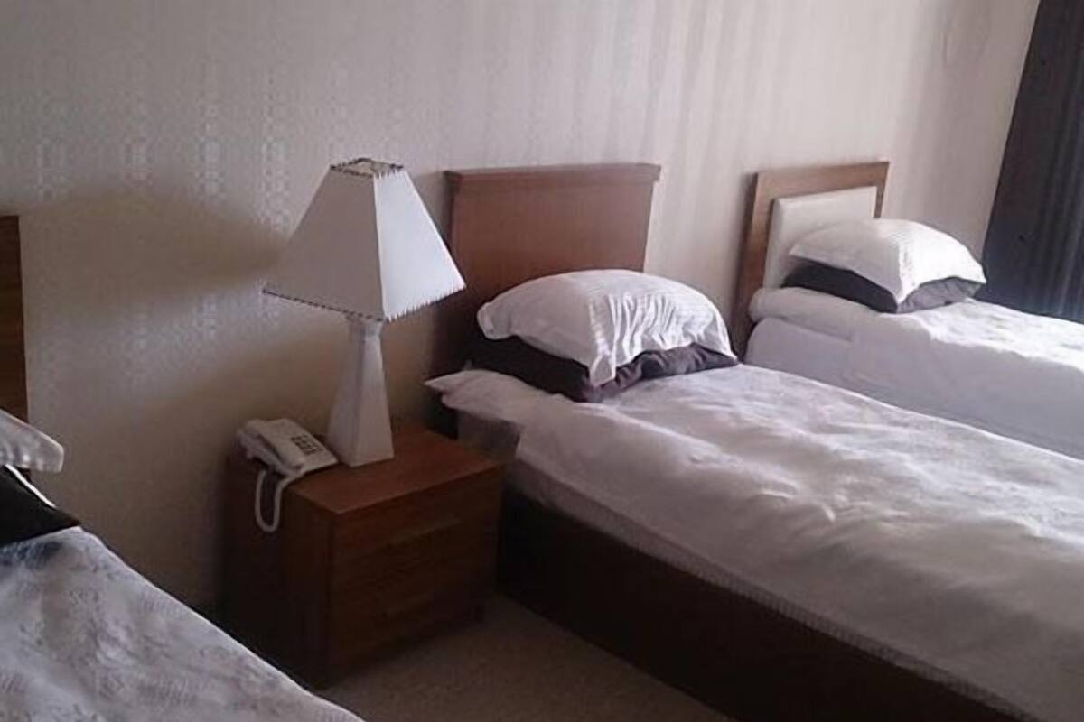 Ein Hotelzimmer mit zwei Einzelbetten, einem Nachttisch mit Lampe und einem Telefon.