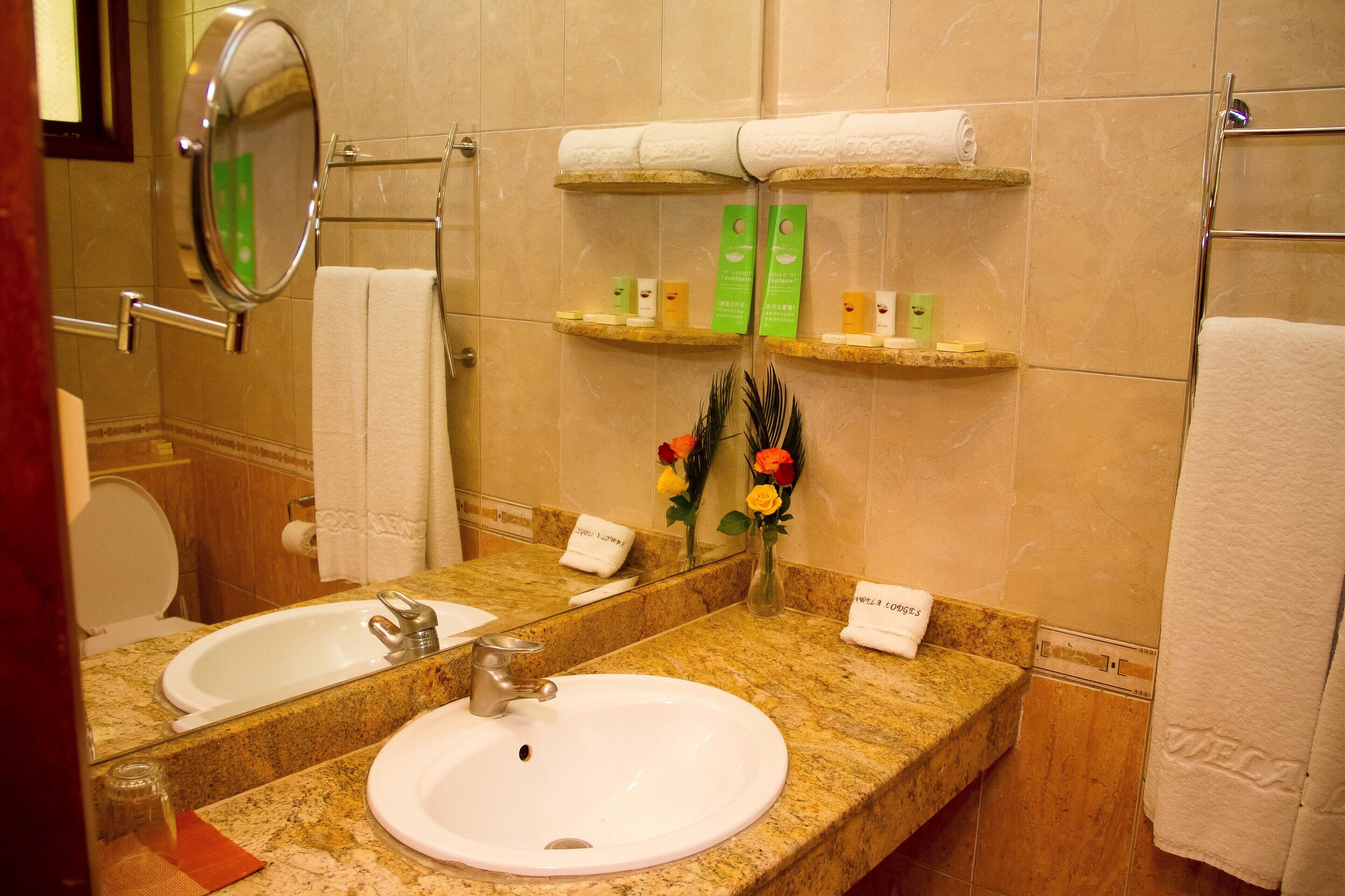 Un baño con lavamanos, espejo, toallero y estantes con artículos de tocador.
