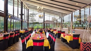 A restaurant with multiple tables and chairs, large windows, and a chandelier. - Sawela Lodge (Naivasha)