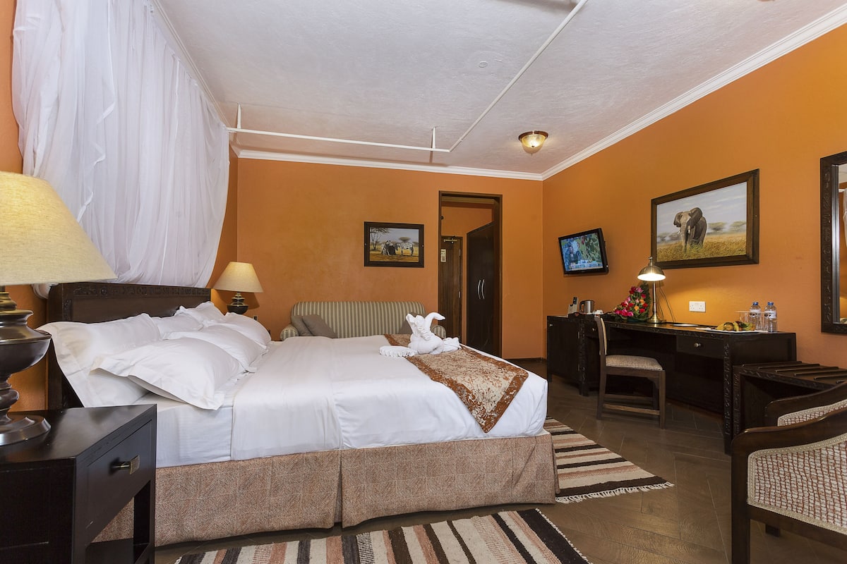 A hotel room with a large bed, a desk, a chair, a lamp, and a picture on the wall.