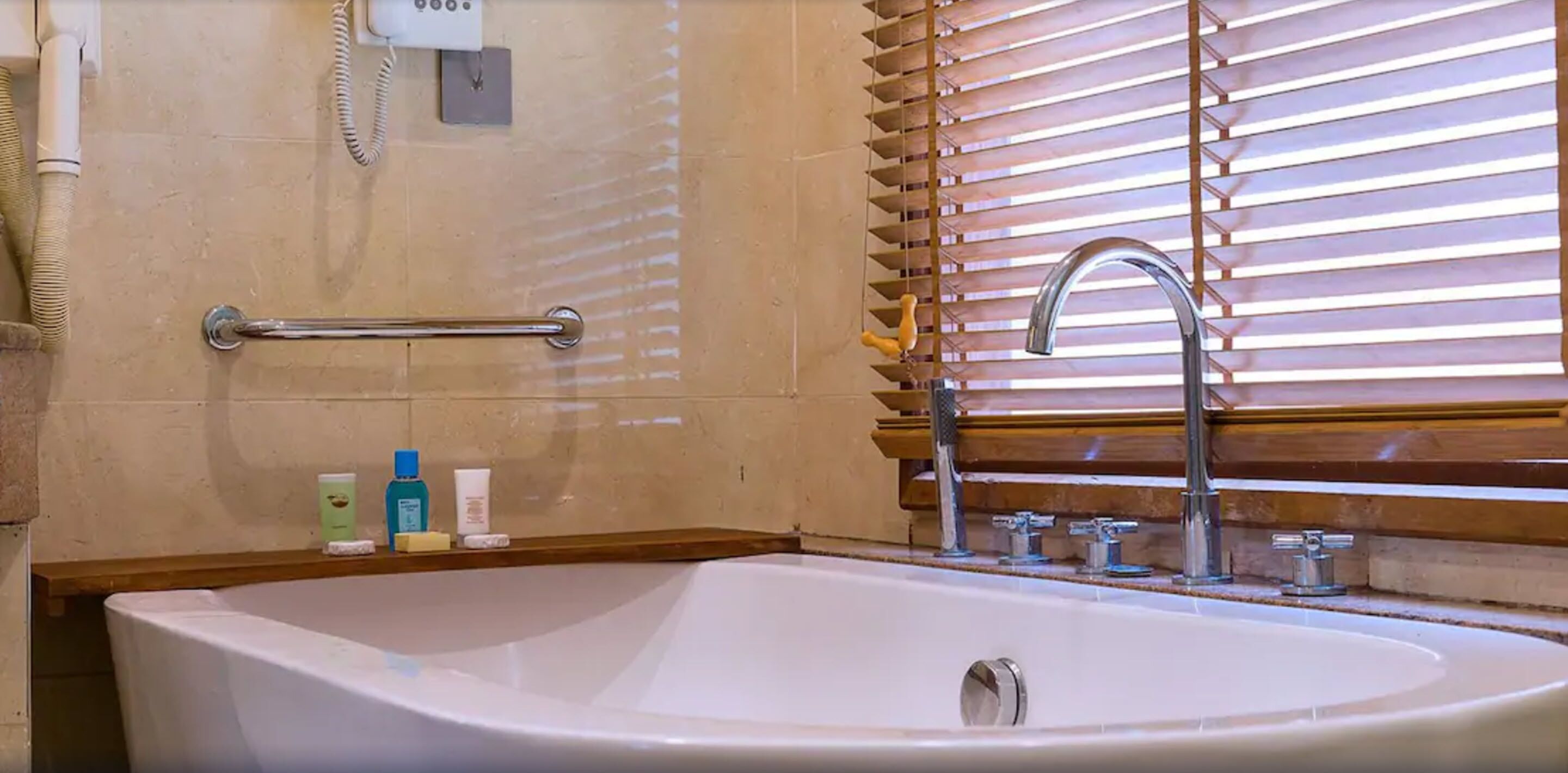 A bathroom with a bathtub, a handrail, a vanity with a sink, and wooden blinds.