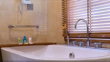 A bathroom with a bathtub, a handrail, a vanity with a sink, and wooden blinds.