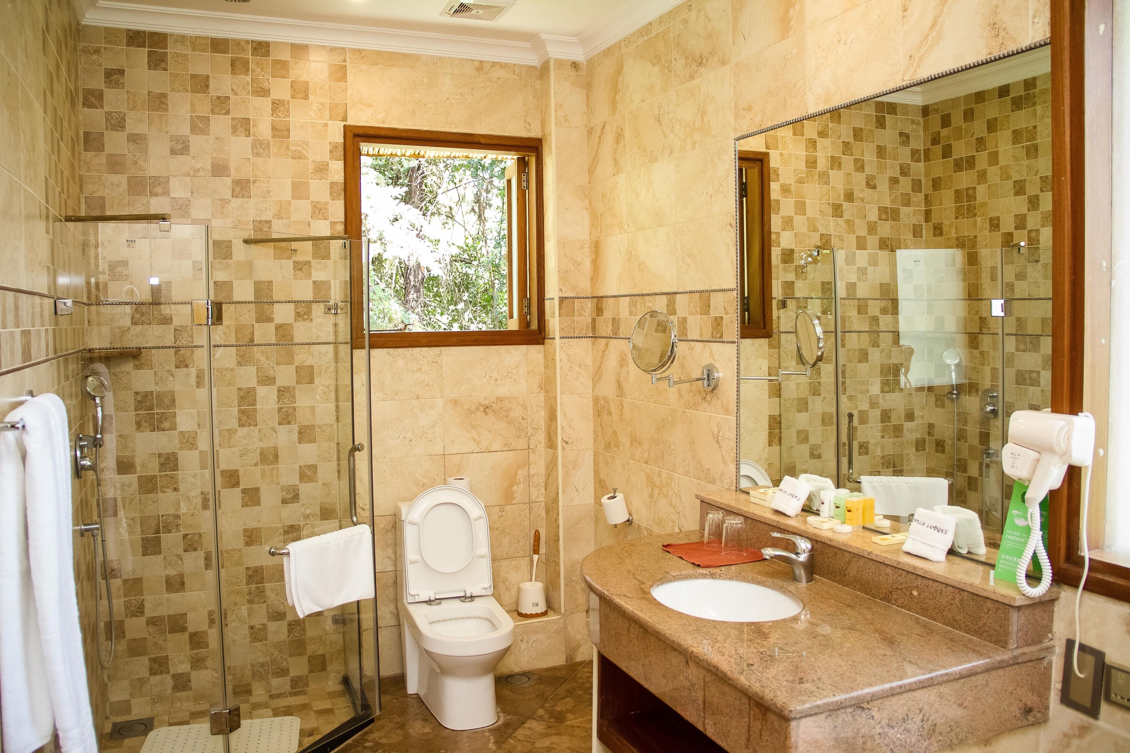 Ein Badezimmer mit Duschkabine, Toilette, Waschbecken mit Spiegel und einem Fenster für natürliches Licht.