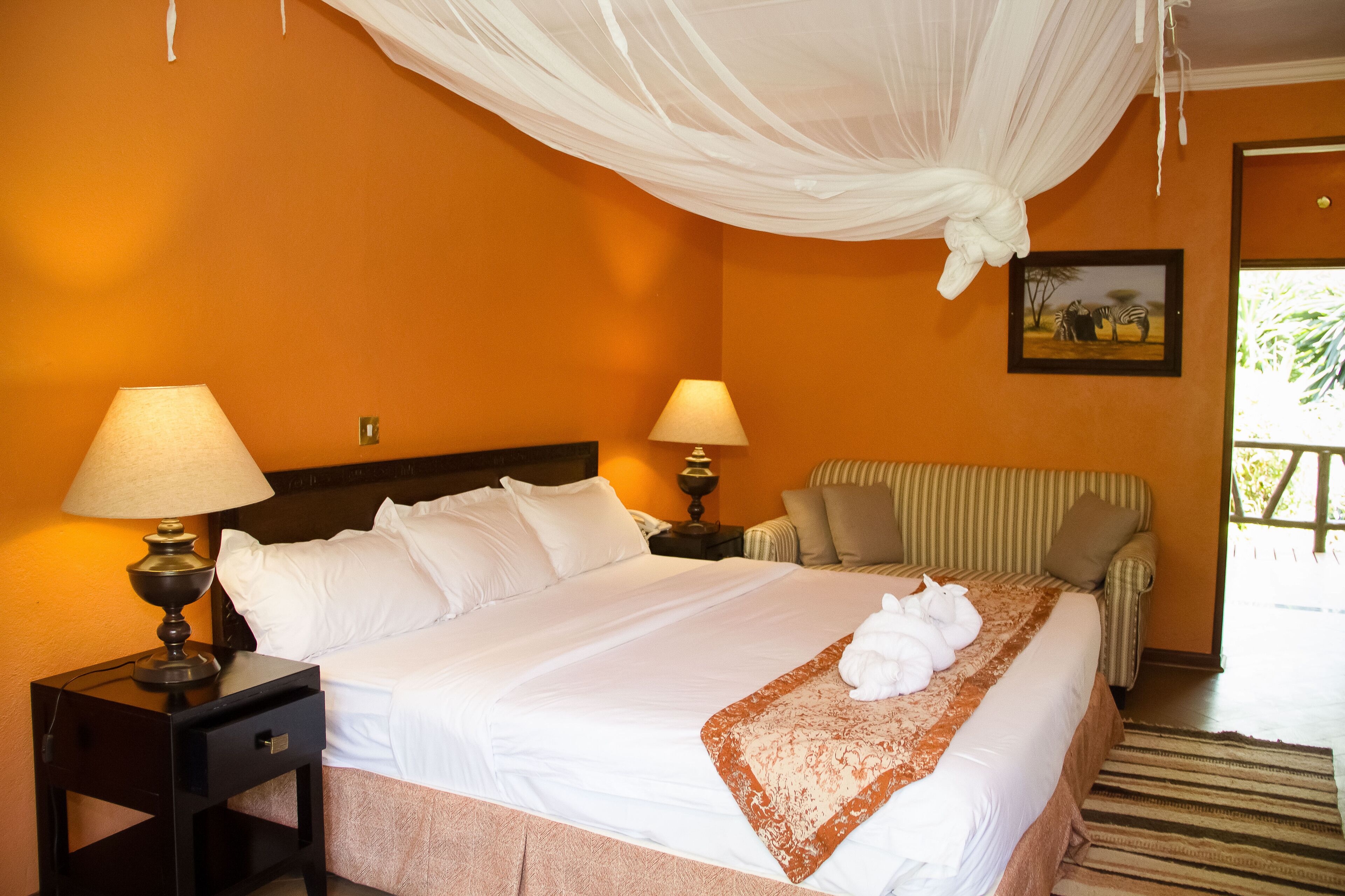A hotel room with a large bed, two bedside lamps, a striped armchair, and a painting on the wall.