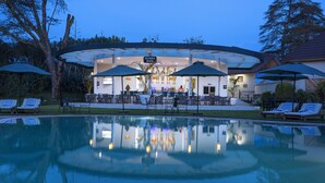 A pool area with lounge chairs and umbrellas, a bar with a zebra-themed sign, and a building with a glass facade. - Sawela Lodge (Naivasha)