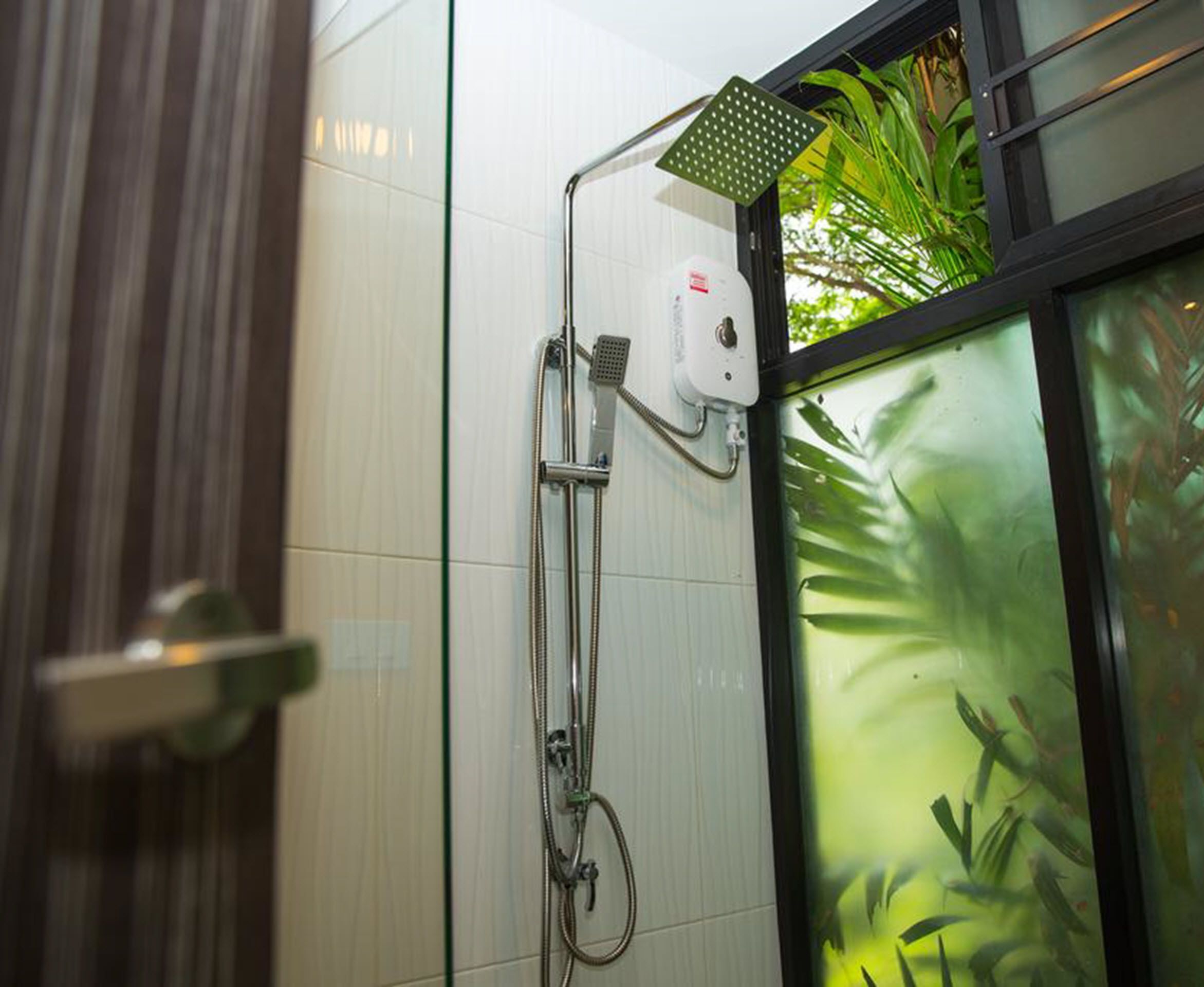 A modern bathroom with a glass shower enclosure, a visible control panel, and a view of indoor plants through the glass.