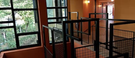 A multi-level interior with a staircase, metal railings, and large windows offering a view of greenery outside.