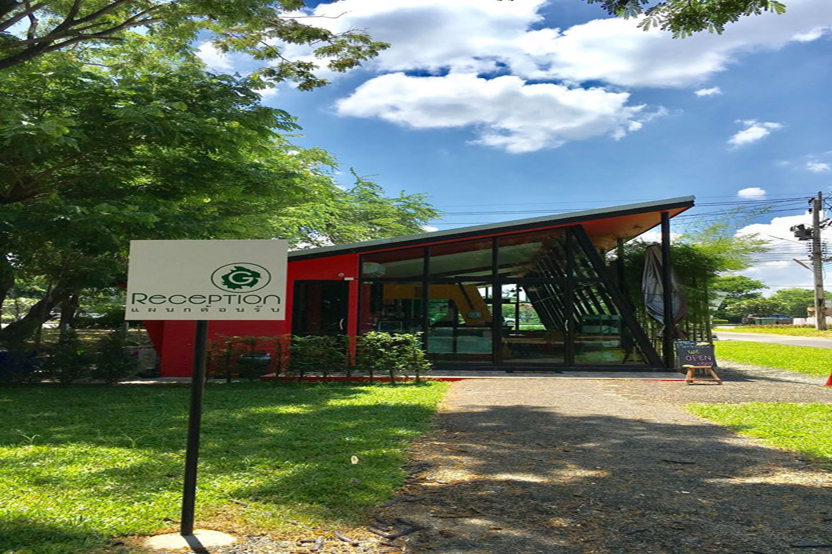 Un área de recepción con un letrero, un edificio moderno con puertas de vidrio y un sendero que conduce a él.