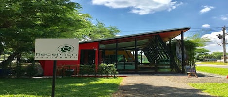 A reception area with a sign, a modern building with glass doors, and a pathway leading to it.