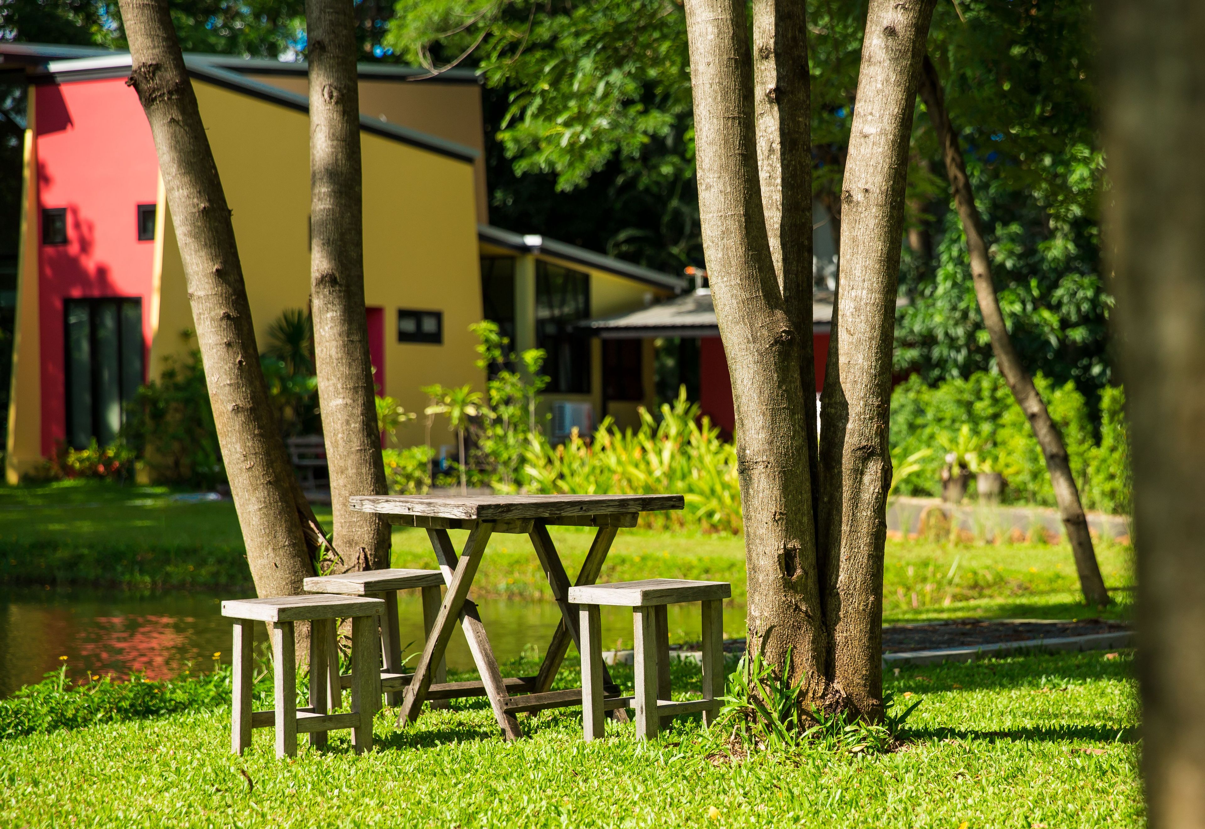 A picnic table with benches in a grassy area with trees and a building in the background.