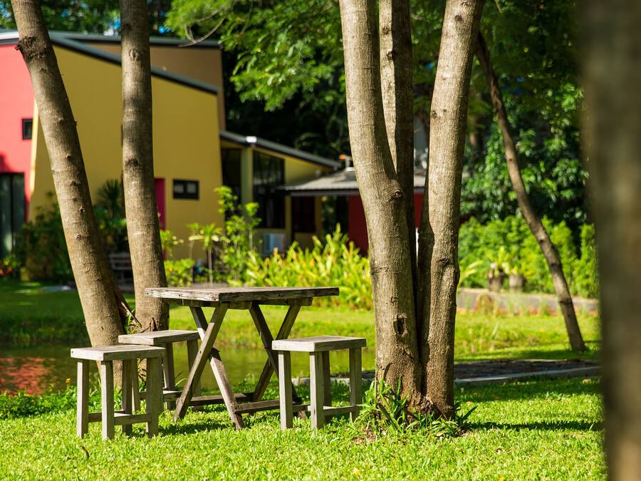 A picnic table with benches in a grassy area with trees and a building in the background.