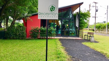 A reception area with a sign, a red building, and a pathway leading to a glass entrance.