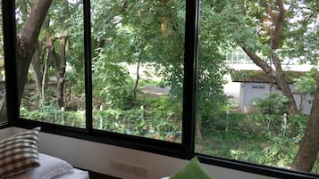 A room with a large window overlooking a garden with trees and a building in the background.