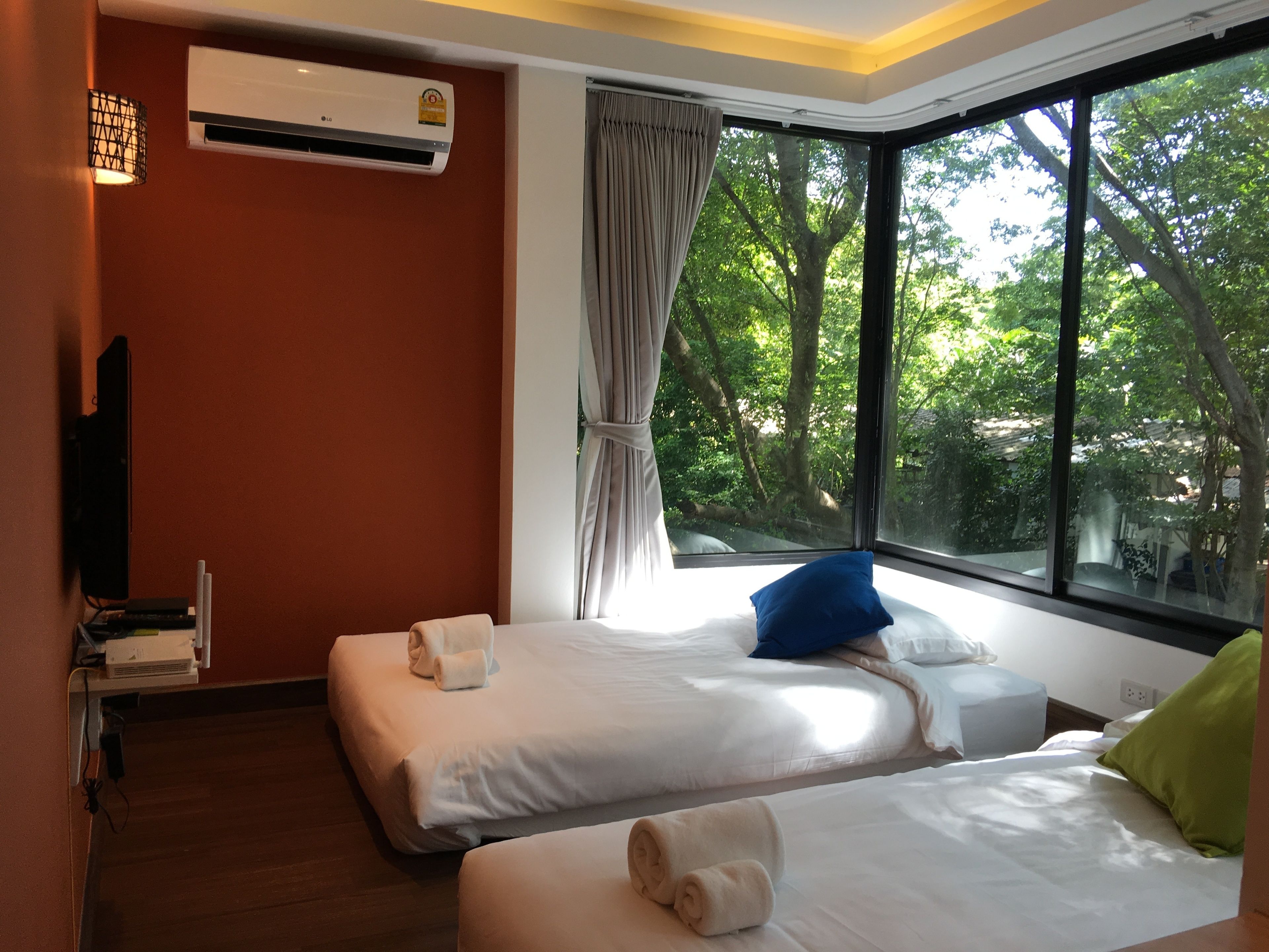 Habitación de hotel con dos camas, televisor, aire acondicionado y ventana con vistas a árboles.