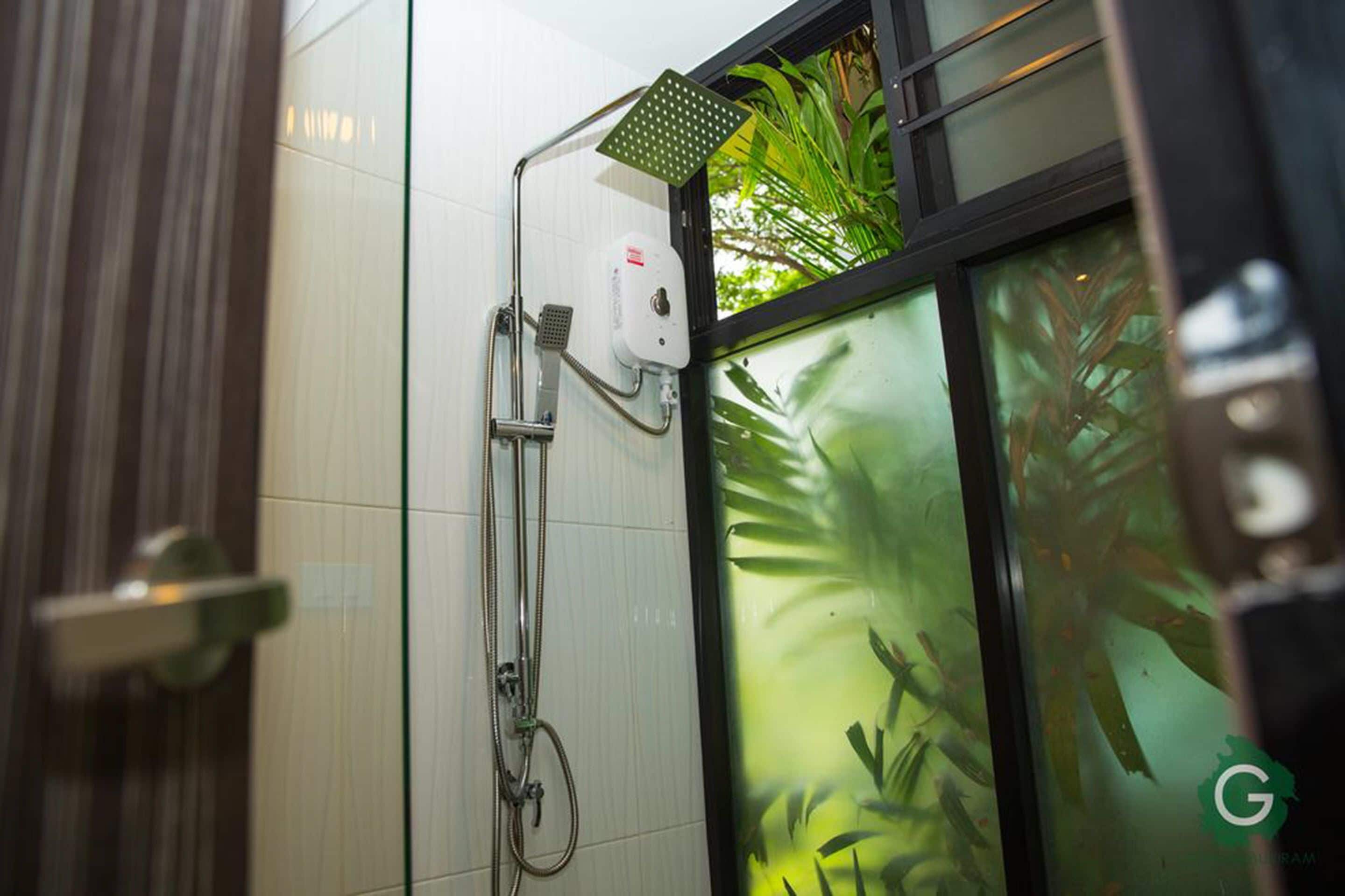A shower area with a handheld showerhead, a wall-mounted control panel, and a glass door with a green plant view.
