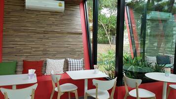A modern indoor seating area with a red and white color scheme, featuring a wooden wall, white tables and chairs, and a view through large windows.