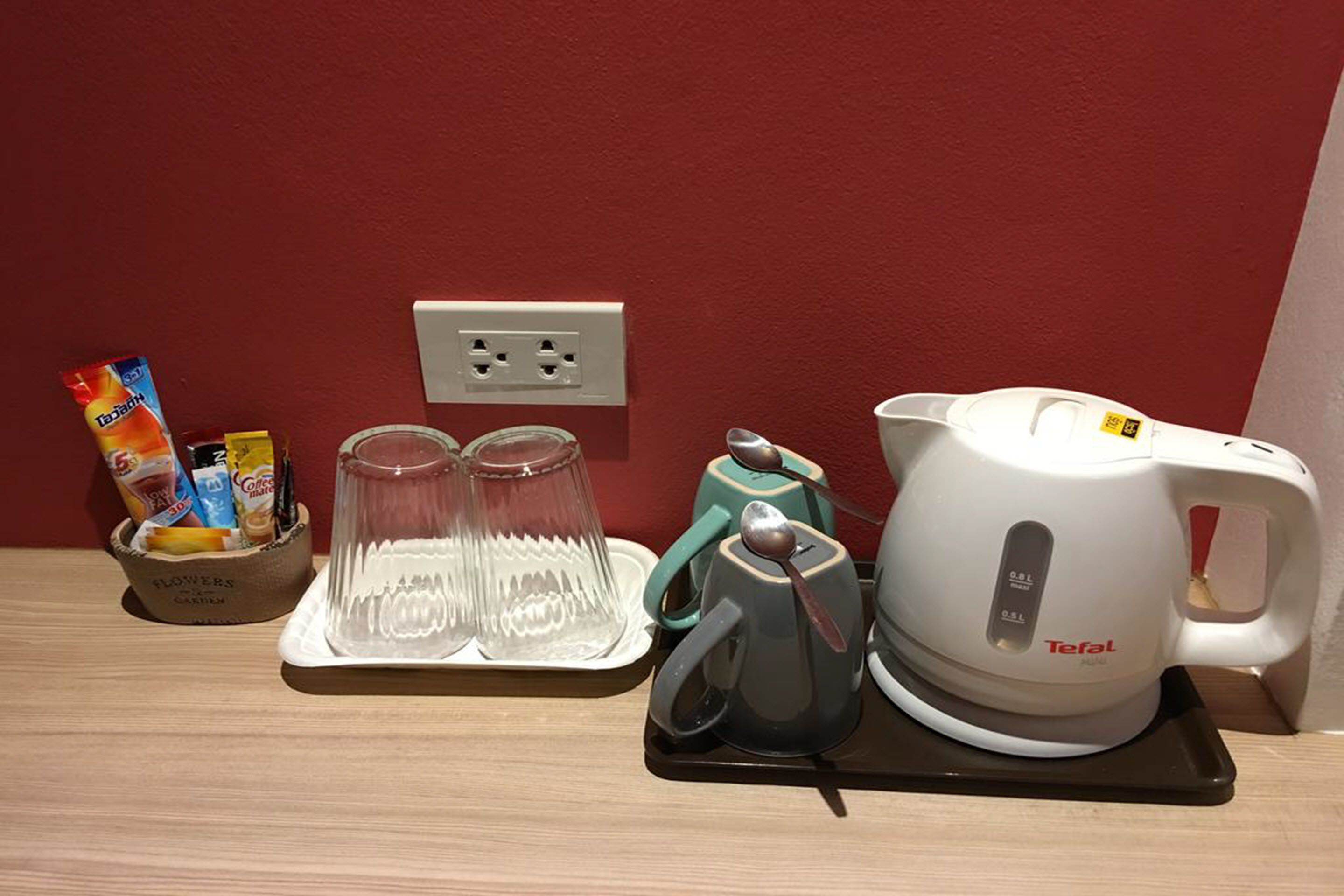 A kitchen area with a coffee maker, two glasses, and a cup on a tray, along with a basket of snacks and a flower vase.