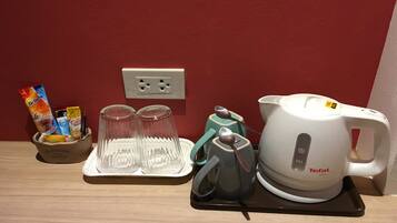 A kitchen area with a coffee maker, two glasses, and a cup on a tray, along with a basket of snacks and a flower vase.
