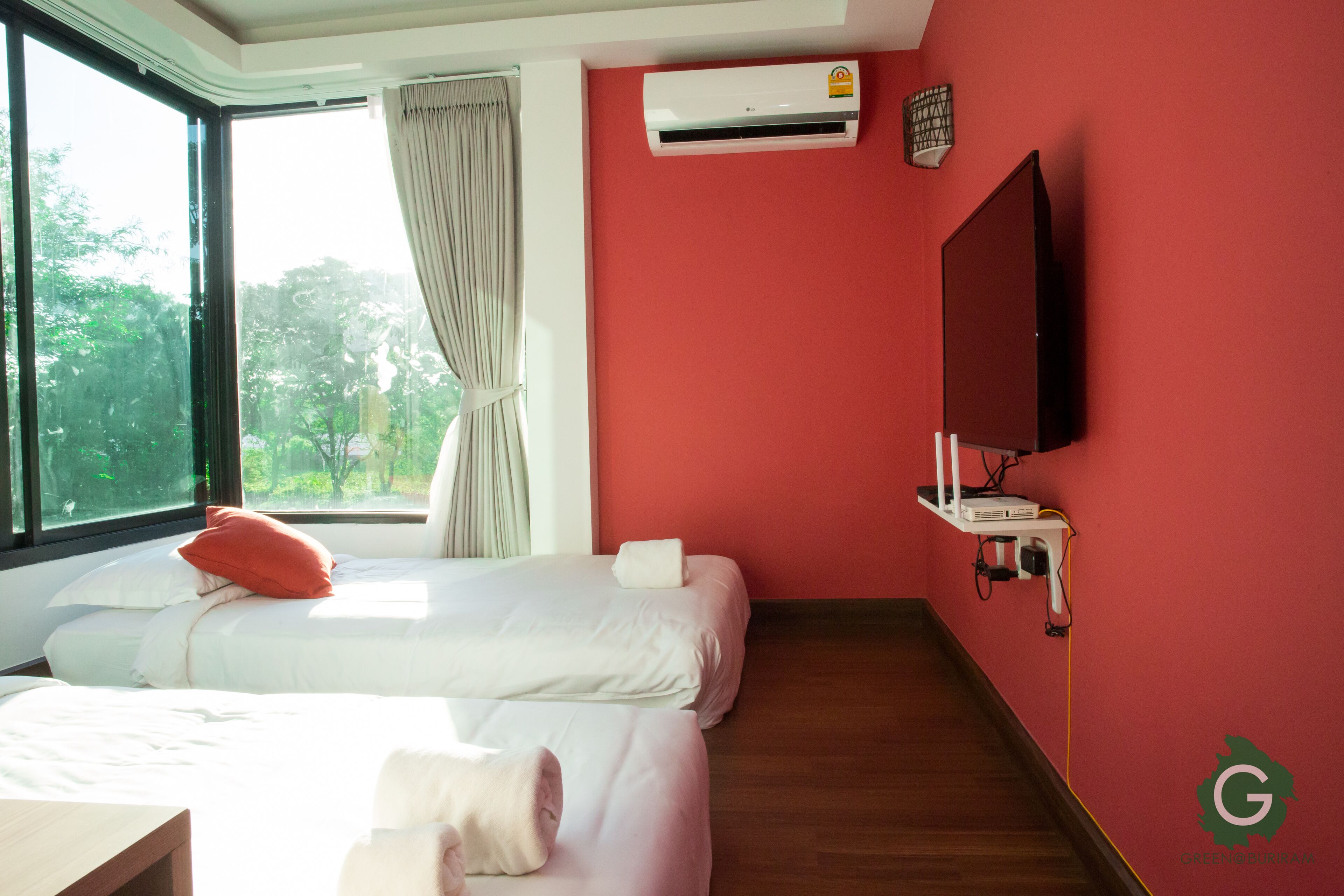 Ein Hotelzimmer mit zwei Betten, einem Fernseher, einer Klimaanlage und einem Fenster mit Vorhängen.