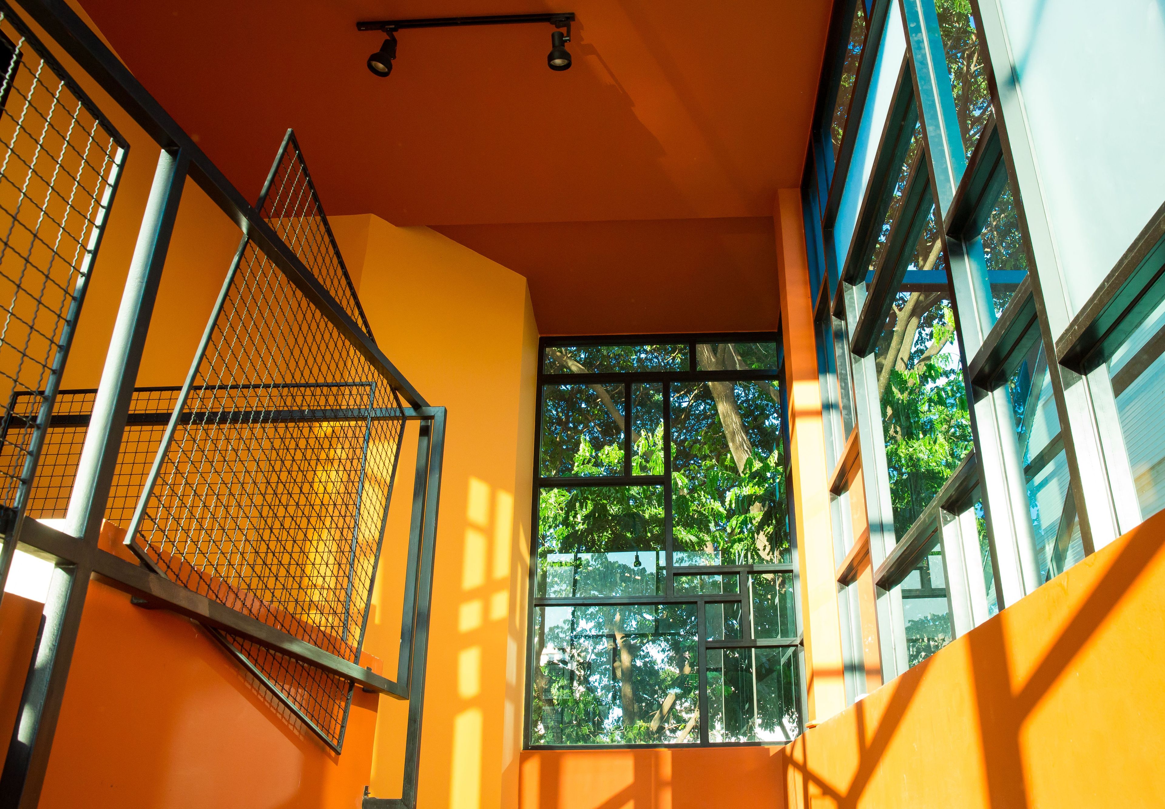 A corridor with orange walls, metal railings, and large windows with views of trees.