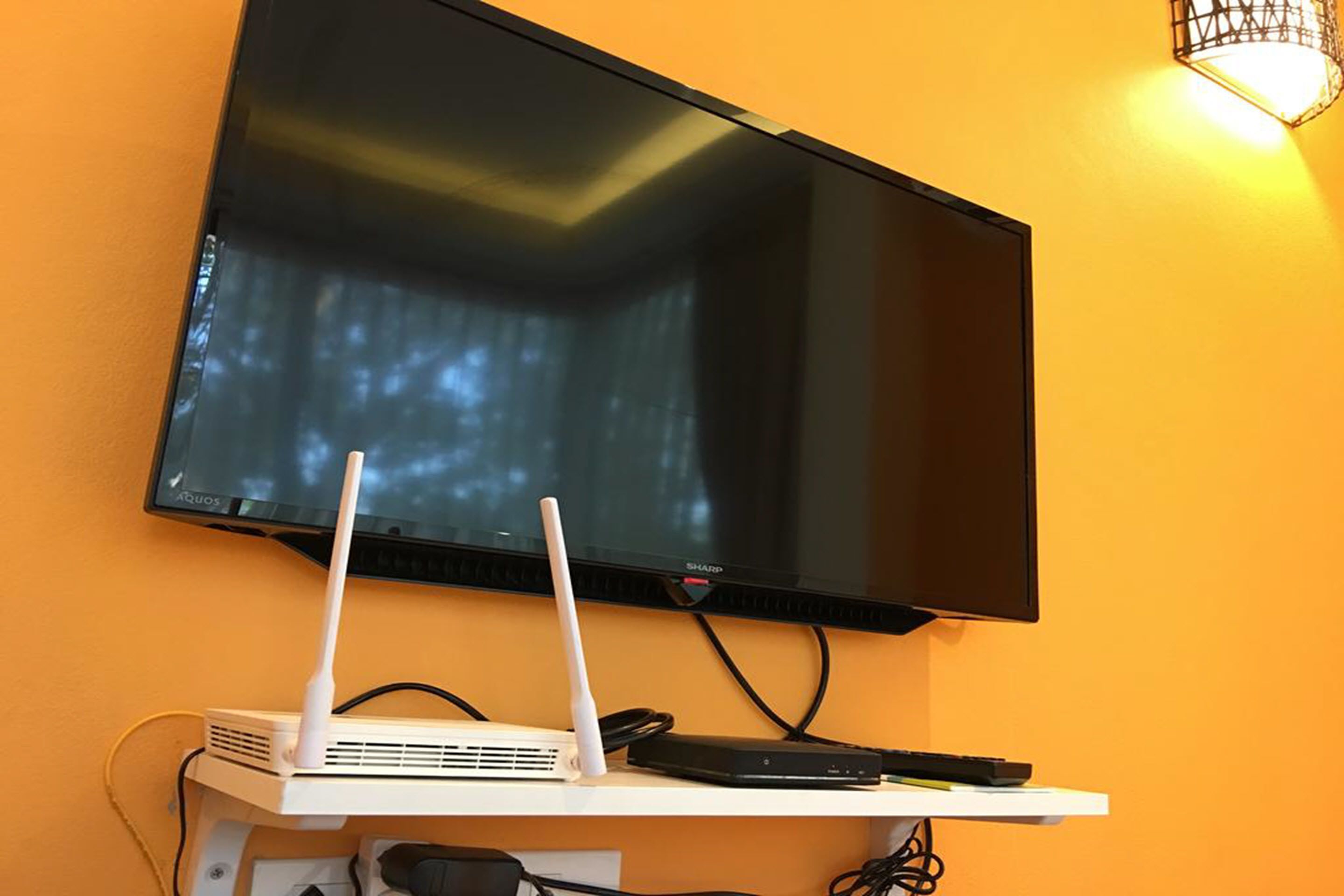 A flat-screen TV mounted on a wall with two white routers on a white shelf below.