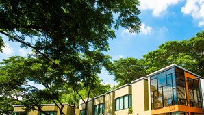 Un edificio moderno con múltiples ventanas y techo plano, rodeado de exuberantes árboles verdes.