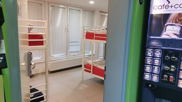 Habitación de hotel con literas, una ventana con persianas, un radiador y una máquina de café.