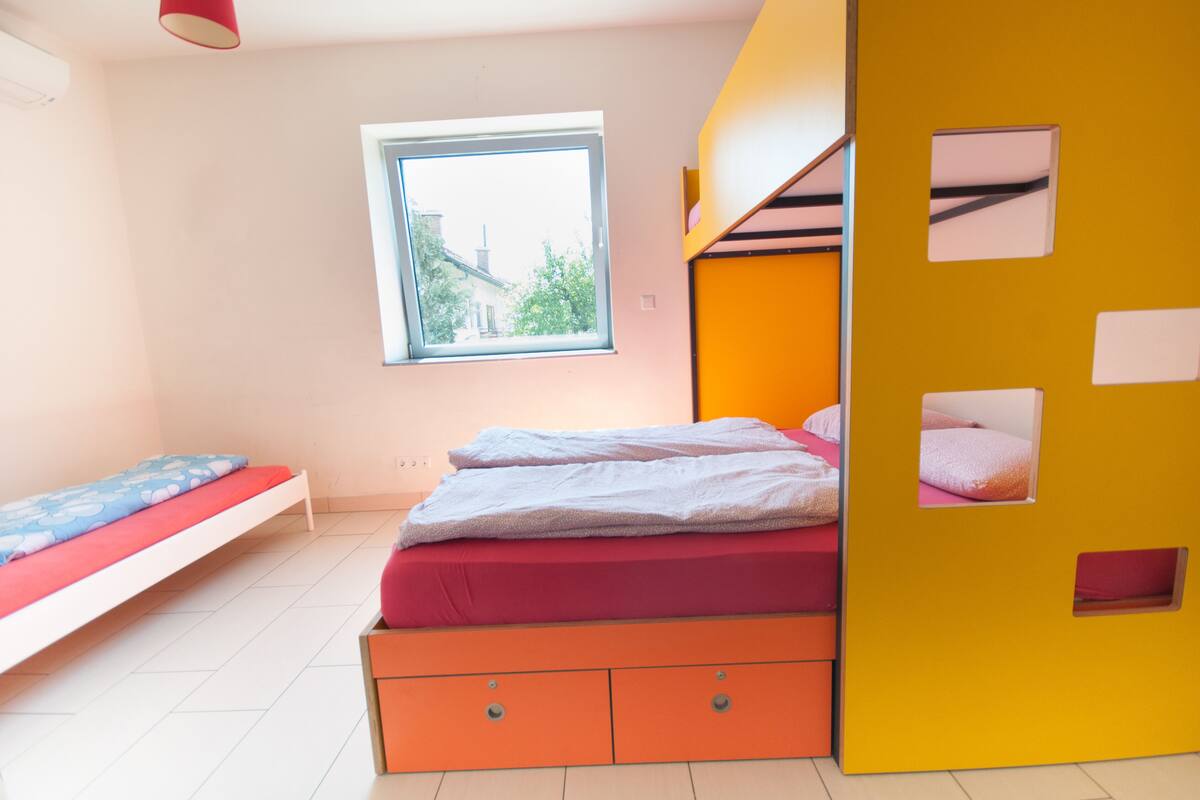 Quarto com beliche, janela e vista para um prédio.