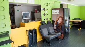 Un café moderno con una decoración verde y amarilla, una recepción, zona de estar y un monitor de computadora.