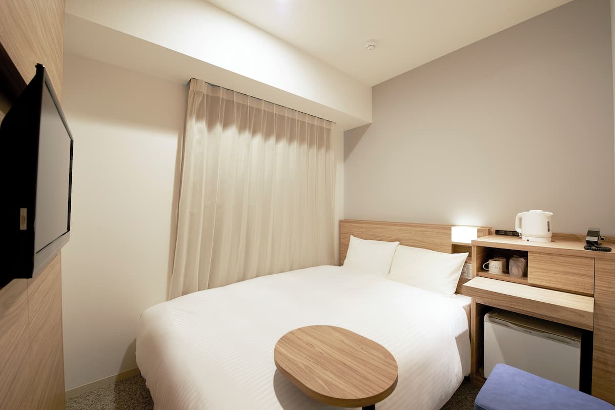 A hotel room with a bed, bedside table, lamp, and a small refrigerator.