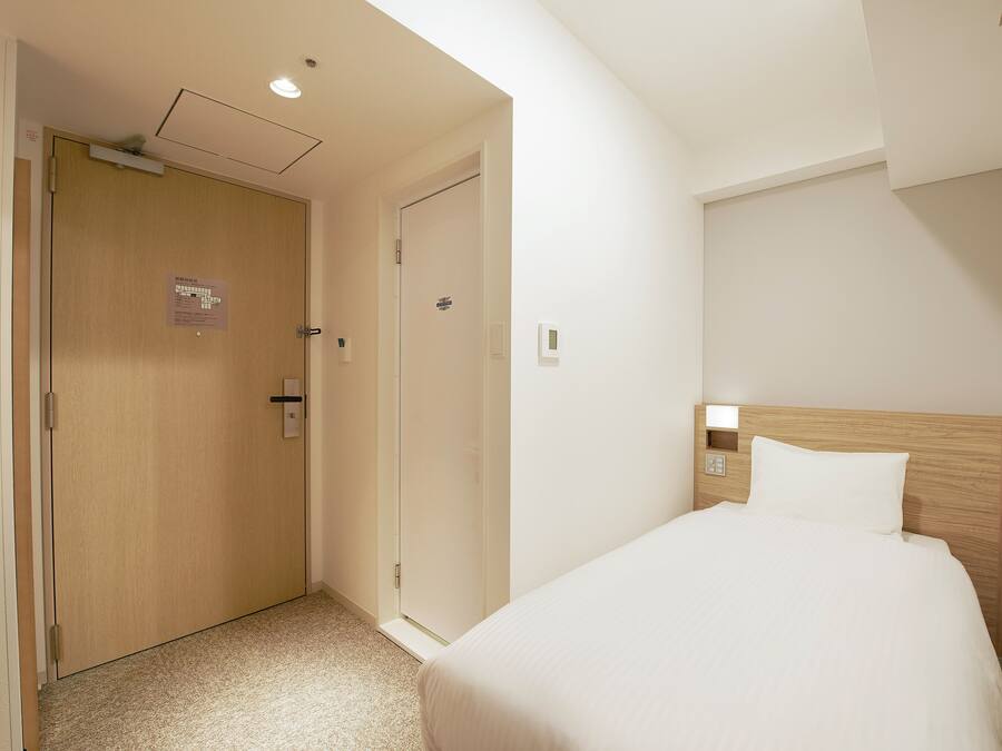 Quarto de hotel com porta de madeira, uma cama com cabeceira de madeira e uma mesa de cabeceira com uma luminária.