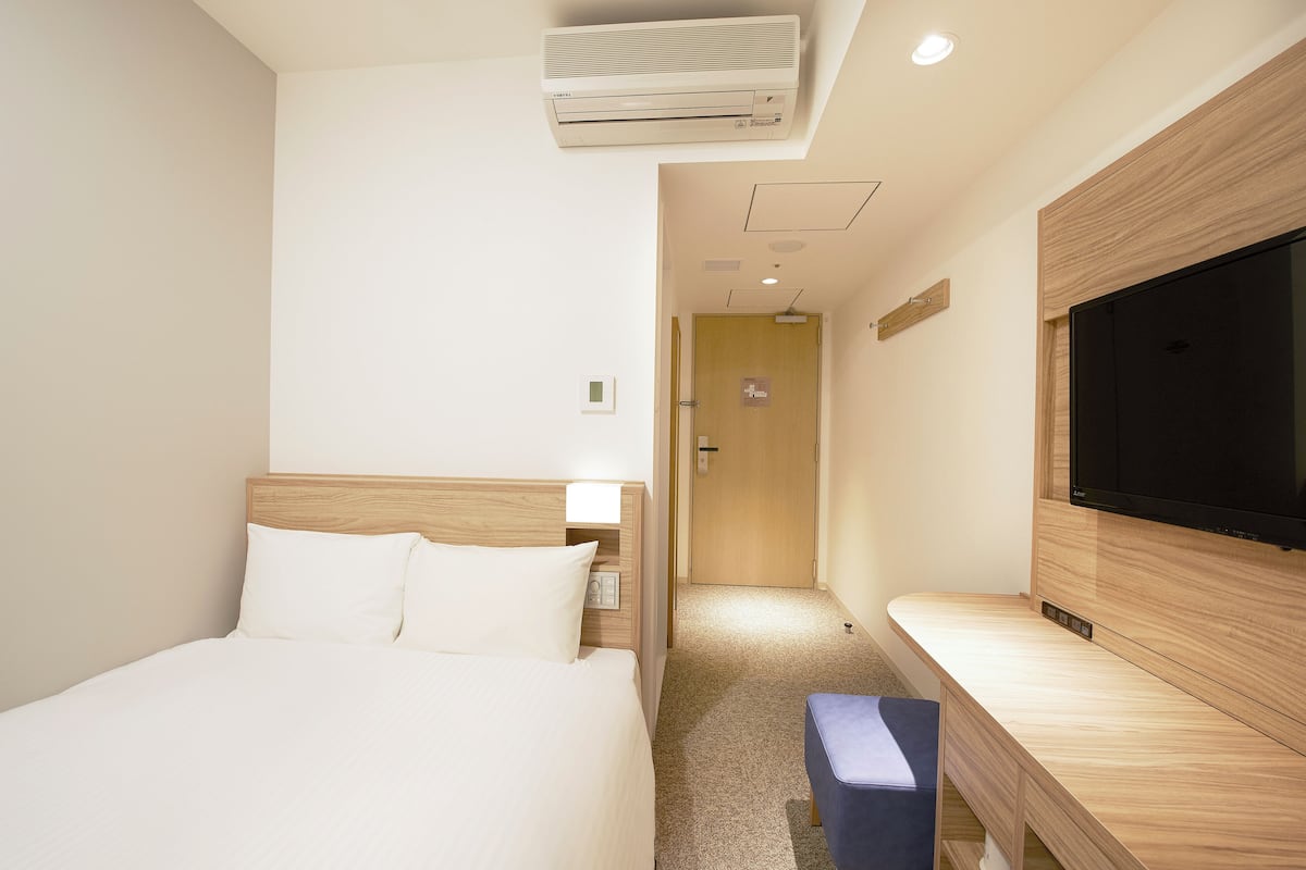 A hotel room with a bed, a TV, an air conditioner, and a small desk.