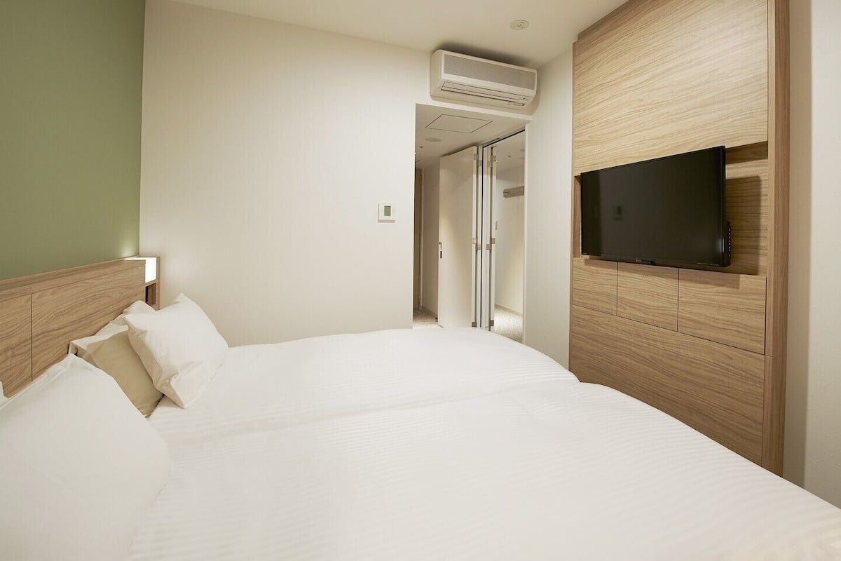 A hotel room with a bed, a television, and a wall-mounted air conditioning unit.
