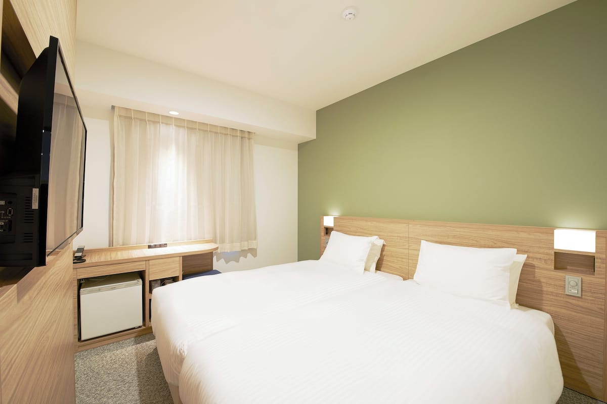 A hotel room with a bed, a desk with a computer, a television, and a window with curtains.