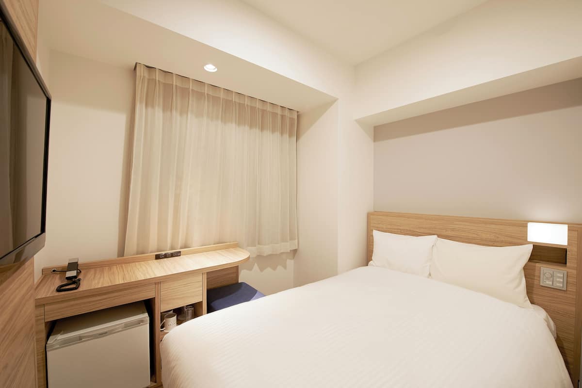 A hotel room with a bed, a desk with a telephone, a small refrigerator, and a television.