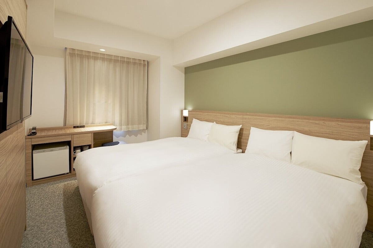 A hotel room with a large bed, a desk with a computer, a TV, and a small fridge.