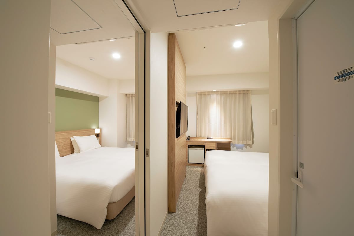 A hotel room with two beds, a desk, a television, and a mirror.