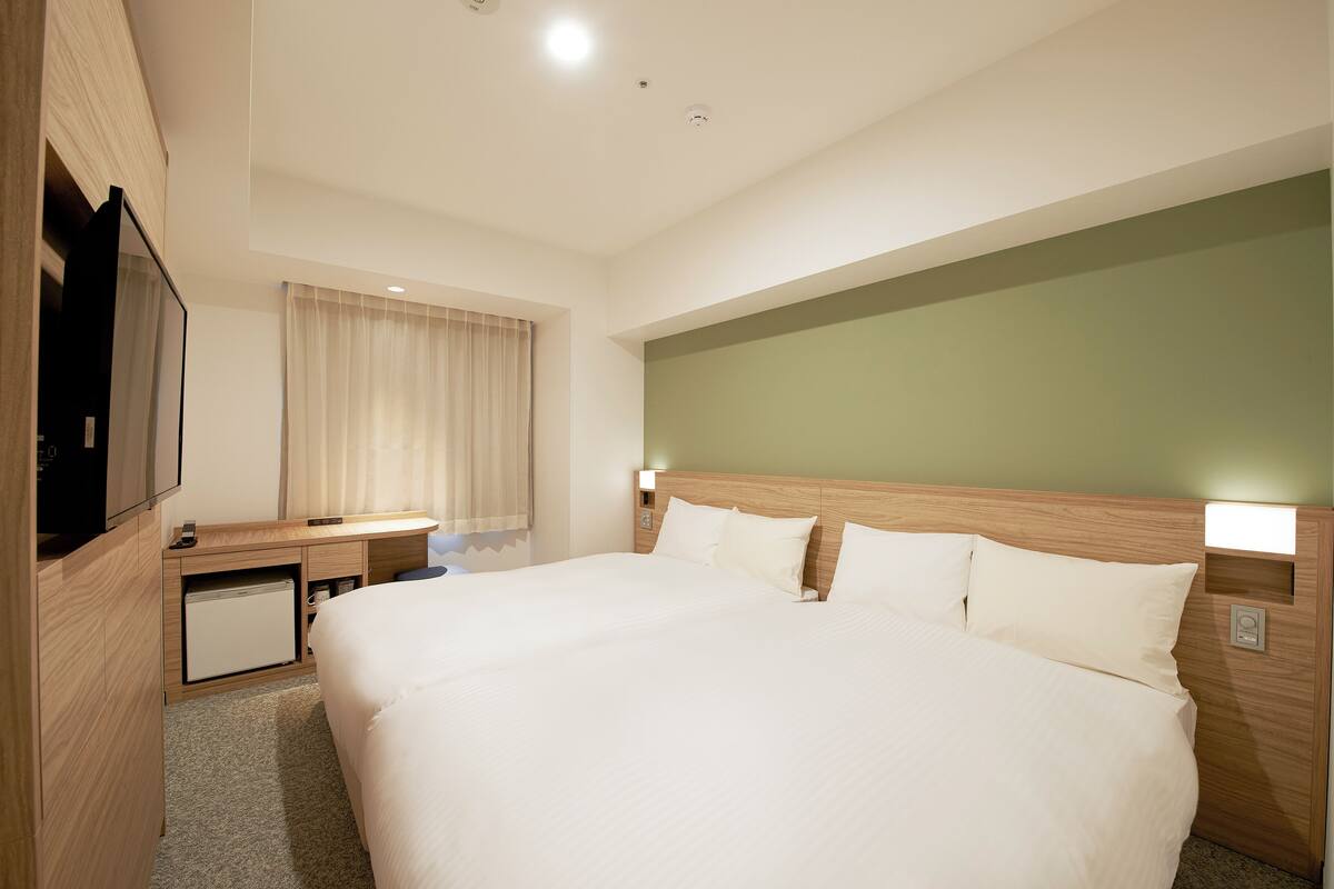 A hotel room with a large bed, a desk with a computer, a television, and a small refrigerator.