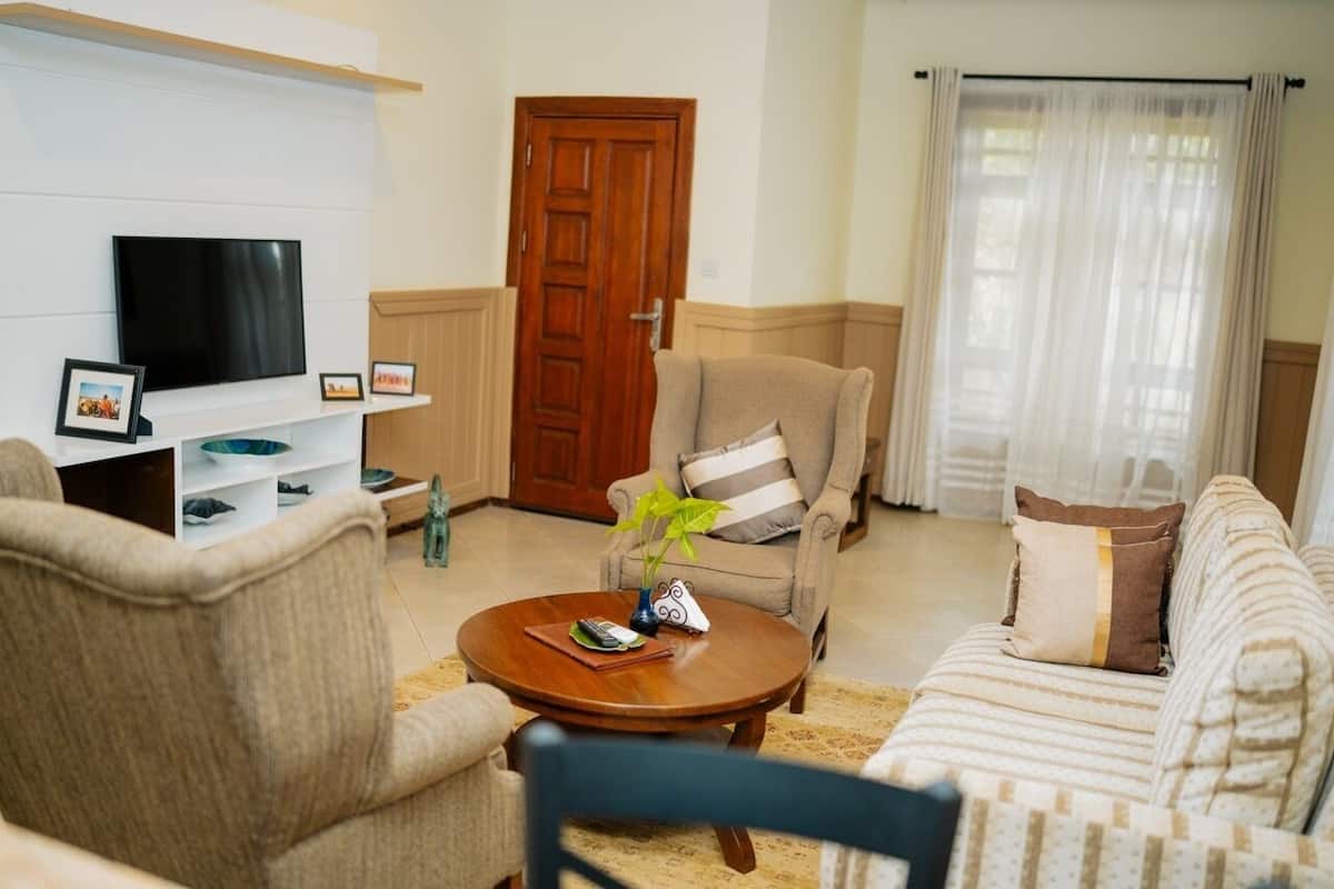Una sala de estar con televisor, sofá, sillón y una mesa de centro con un jarrón.