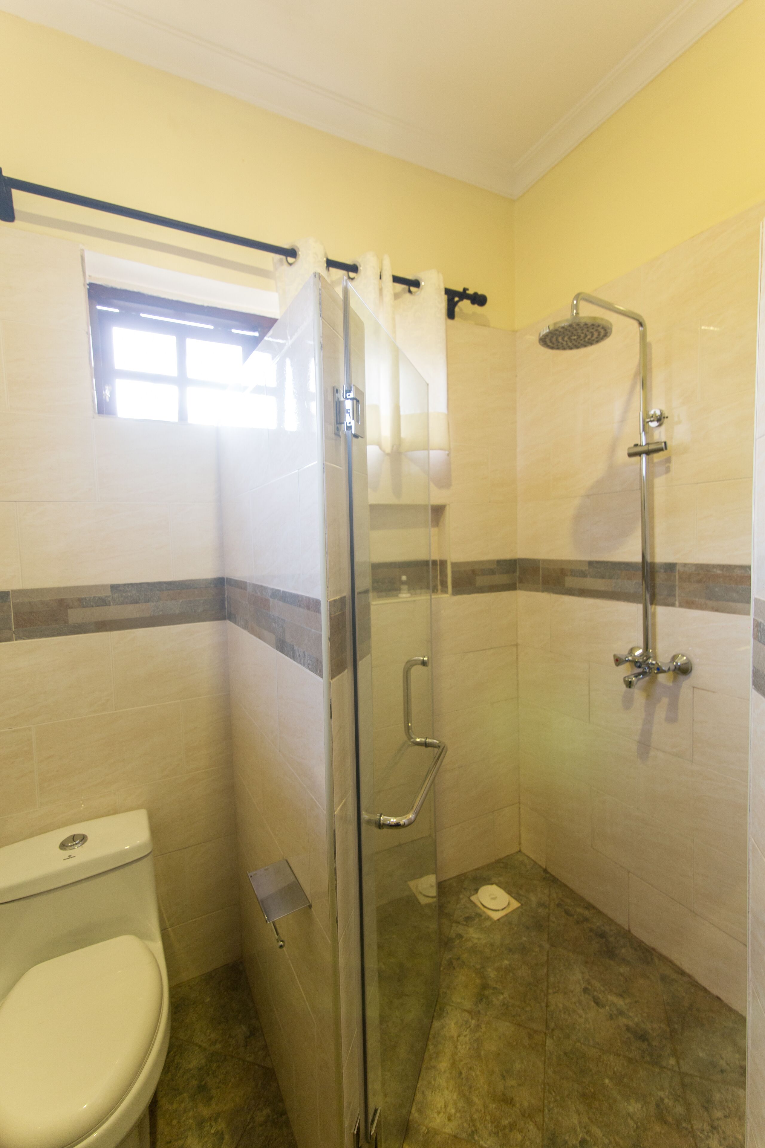 Un baño con ducha de vidrio, inodoro y ventana sobre el lavamanos.