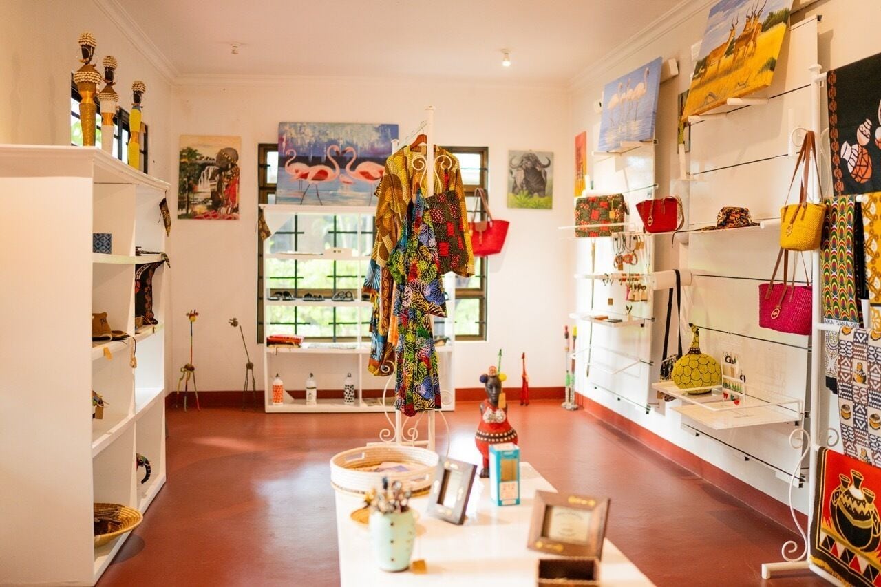 Een lobby van een boetiekhotel met een centraal uitstal van kleurrijke textiel en accessoires, planken met diverse items en kunstwerken aan de muren.