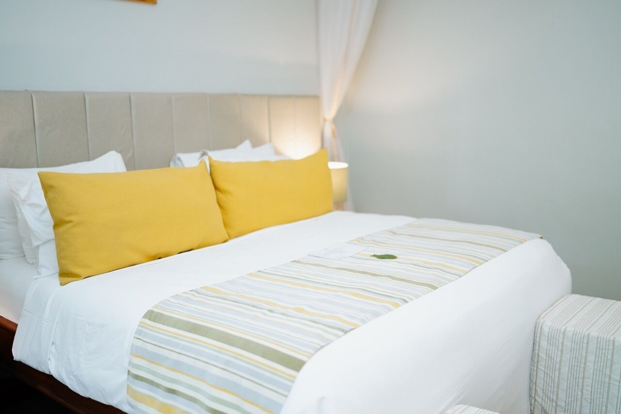 A neatly made bed with white and yellow bedding, a striped blanket, and a headboard against a light-colored wall.