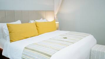 A neatly made bed with white and yellow bedding, a striped blanket, and a headboard against a light-colored wall.